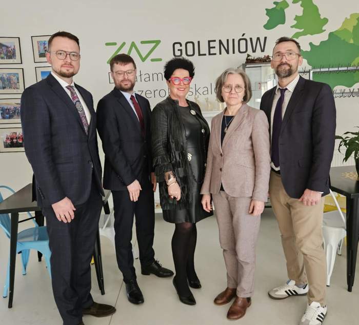 Pokaż zdjęcie: Na zdjęciu jest 5 osób, w środku dwie Panie. Pozują do zdjęcia. W tle Zielono czarny napis ZAZ Goleniów i grafika z zieloną mapą