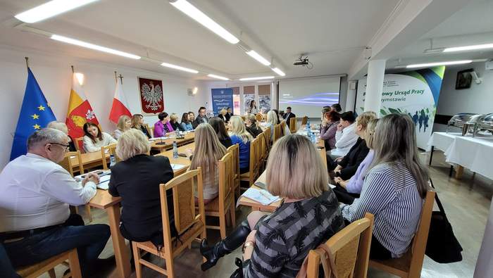 Pokaż zdjęcie: W sali konferencyjnej przy dużym stole siedzą zaproszeni goście.