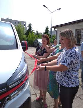 Pokaż zdjęcie: Trzy kobiety przecinają czerwoną wstęgę, którą obwiązany jest biały samochód