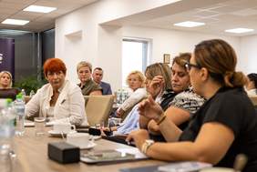 Pokaż zdjęcie: Przy stole siedzą uczestnicy spotkania w większości kobiety.