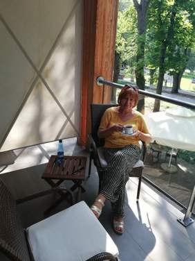 Uśmiechnięta kobieta siedząca na fotelu trzymająca filiżanke z kawą