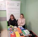 Stoisko informacyjne PFRON w placówce ZUS – dwie osoby siedzą przy stoliku z materiałami i ulotkami. W tle roll-up CIDON. Punkt udzielania porad dla osób z niepełnosprawnościami podczas dyżuru eksperckiego.