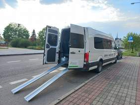 Pokaż zdjęcie: biały autobus z otwartymi z tyłu drzwiami z których wysuwają się najazdy do wózka inwalidzkiego.