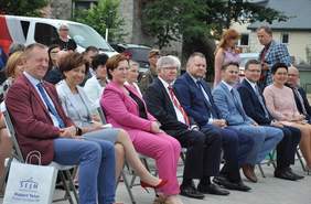 Pokaż zdjęcie: Siedząca na krzesłach grupa gości, w tym Pani Minister Rodziny i Polityki Społecznej oraz Parlamentarzyści
