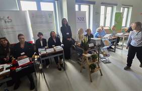 Przy stoiskach eksperckich siedzą przedstawicielki instytucji. W tle widać banery.