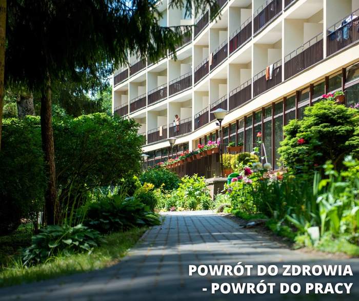 Pokaż zdjęcie: Budynek wśród zieleni. Na ścianie budynku widoczne liczne okna i balkony.