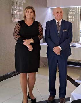 Pokaż zdjęcie: Dwie osoby, kobieta i mężczyzna stoją w sali restauracyjnej i rozmawiają.