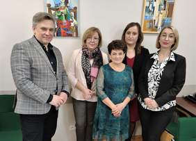 Pokaż zdjęcie: Cztery kobiety i jeden mężczyzna pozują w sali konferencyjnej na tle obrazów. Wszyscy są elegancko ubrani i uśmiechnięci