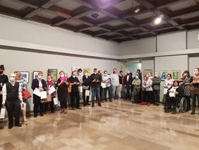 osoby biorące udział w wydarzeniu stoją na tle dwóch ścian na których wiszą różne obrazy ok 20 osób