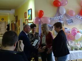 Pokaż zdjęcie: Zdjęcie 4 osób, mężczyzna w garniturze i kobieta z krótkimi czarnymi włosami wręczają podziękowania dwóm paniom, przedstawicielkom PFRON Oddział Lubelski w Lublinie. 