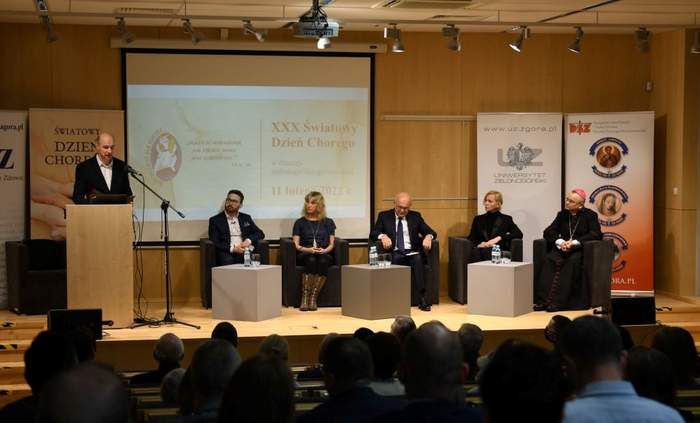 Pokaż zdjęcie: Uczestnicy obchodów w Bibliotece Uniwersytetu Zielonogórskiego siedzą na fotelach na tle rollapów, a konferansjer stoi przy mównicy