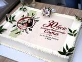 Biały tort jubileuszowy z napisem „30 lat Centrum Pomocowego Caritas”, ozdobiony zielonymi gałązkami, kwiatami i okrągłą grafiką. Tort ustawiony jest na stole.
