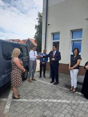 Pokaż zdjęcie: Dyrektor Oddziału Lubuskiego przekazuje kluczyki do nowego auta Burmistrzowi Strzelec Krajeńskich na posesji przed budynkiem ŚDS w obecności zgromadzonych uczestników