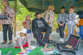 Pokaż zdjęcie: Dyrektor Marta Mordarska wraz z artystami: Stanisławem Kmiecikiem i Martynką Grucą. Artyści malują stopami. Dookoła stoją uczestnicy wydarzenia. Fot: Damian Radziak