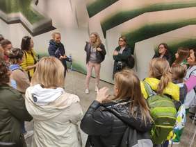 Pokaż zdjęcie: Grupa osób ustawioną w krąg wokół prowadzącej zajęcia