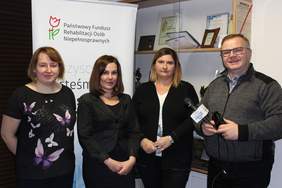 Pokaż zdjęcie: trzy kobiety pracownice Oddziału Lubelskiego PFRON oraz ks. redaktor Wojciech Iwanicki stoją na tle logo PFRON