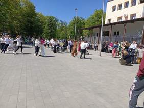 Pokaż zdjęcie: Na parkingu domu kultury grupa osób tańczy w kółku parami. 