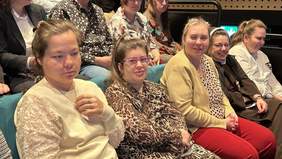 Pokaż zdjęcie: Goście spotkania siedzą w sali kinowej i są uśmiechnięci i zadowoleni