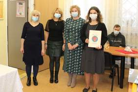 Pokaż zdjęcie: Cztery kobiety, jedna z nich trzyma dyplom na którym widzimy czerwone serce na niebieskim kółku