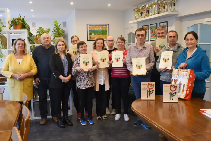 Pokaż zdjęcie: Do pamiatkowego zdjęcia w jednej zsal terapeutycznych zaponowali laureaci konkursu plastycznego wraz z dyrekcją WTZ oraz gośćmi z PFRON. Laureaci trzymają w rękach pamiątkowe dyplomy, grupa ok. 11 osób.