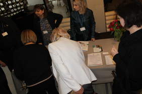 Pokaż zdjęcie: Stół przy którym stoją osoby chcące zapisać się na konferencję.