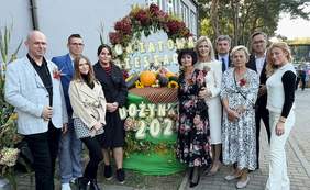 Pokaż zdjęcie: Do zdjęcia pozuje grupa osób: kobiet i mężczyzn. Wszyscy są elegancko ubrani. Między nimi znajduje się dekoracja z napisem: "Powiatowa Biesiada Dożynkowa 2026". 