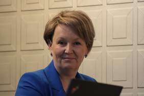 Pokaż zdjęcie: Kobieta blondynka z krótkimi włosami, ubrana w niebieska marynarkę, lekko się uśmiecha i spogląda w obiektyw