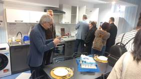 Pokaż zdjęcie: Zdjęcie kuchni w której zaproszone osoby zaglądają do szafek, oglądają wyposażenie.