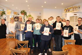 Pokaż zdjęcie: Zdjęcie grupy osób stojących przed stołami, trzymających w dłoniach dyplomy