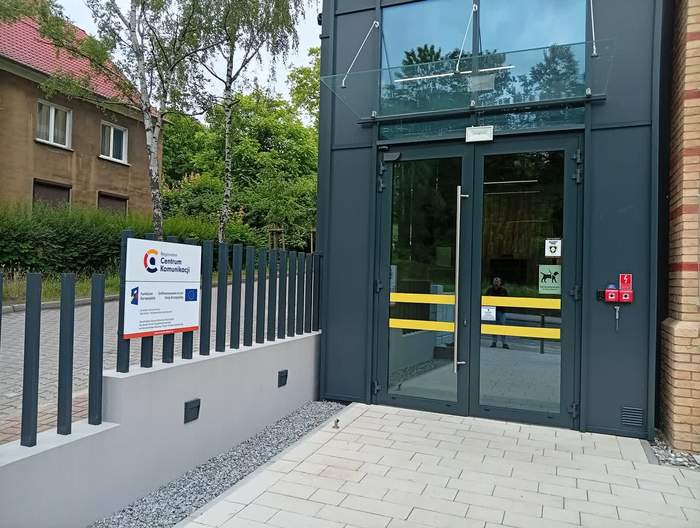 Pokaż zdjęcie: Widoczne nowoczesne wejscie do budynku oraz tablica z logo Centrum