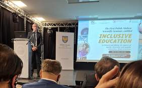 Pokaż zdjęcie: Sala konferencyjna z ekranem, na którym wyświetlana jest prezentacja opatrzoną logo PFRON. Z lewej strony mężczyzna przemawiający z mównicy do mikrofonu. Przed nim zgromadzona publiczność.