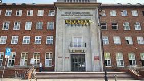 Pokaż zdjęcie: Budynek Urzędu Marszałkowskiego Województwa Pomorskiego. Centralnie umieszczone wejście, nad nim flagi i nazwa urzędu. Budynek z czerwonej cegły, symetryczny, z wieloma oknami. 