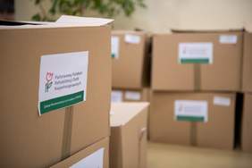 Pokaż zdjęcie: Pudełka oznakowane logotypem PFRON, przygotowane do przekazania osobom potrzebującym.