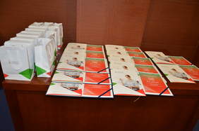 Pokaż zdjęcie: Stolik reprezentacyjny PFRON z dyplomami i upominkami dla uczestników konkursu na najlepsze prace naukowe o tematyce niepełnosprawności.