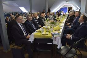 Pokaż zdjęcie: podłużne stół na którym serwowane są potrawy wielkanocne, przy stole siedzi duża grupa osób  