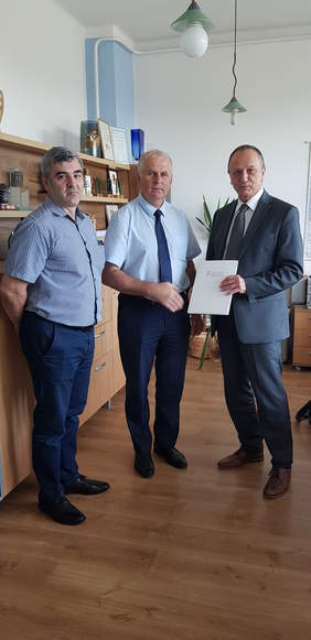 trzej mężczyźni stoją, jeden wręcza dokumenty