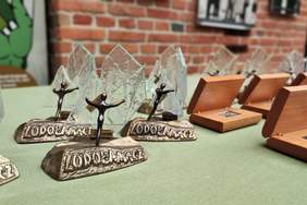 Pokaż zdjęcie: Ustawione na stoliku statuetki w konkursie Lodołamacze 2022. Statuetki kształtem przypominają człowieka dzwigającego  duży kawał lodu.