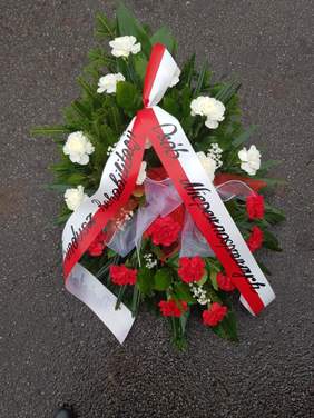 Pokaż zdjęcie: Na asfalcie leży biało-czerwona wiązanka kwiatów. Znajduje sie na niej szarfa z napisem: Państwowy Fundusz Rehabilitacji Osób Niepełnosprawnych. 