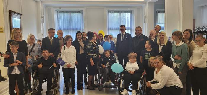 W holu Sejmu liczne grono osób z niepełnosprwanościami, pozują do zdjęcia, są zadowoleni i uśmiechnięci, ubrani odświętnie