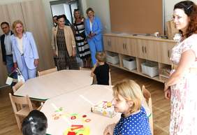 Pokaż zdjęcie: W sali przy okrągłym stoliku siedzą dzieci, zaproszone osoby zwiedzają sale.