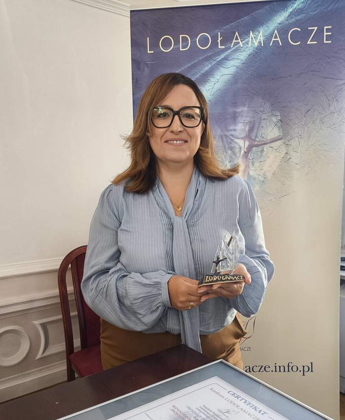 Pokaż zdjęcie: Kobieta w niebieskiej bluzce pozuje do zdjęcia trzymając w ręku statuetkę lodołamacza.