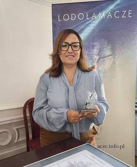 Pokaż zdjęcie: Kobieta w niebieskiej bluzce pozuje do zdjęcia trzymając w ręku statuetkę lodołamacza.