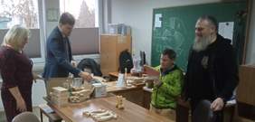 Pokaż zdjęcie: Dyrektor Bogumiła Bzdera pokazuje pracownie stolarską dyrektorowi PFRON, Mateuszowi Szkaradzińskiemu. Na stole leżą drewniane Anioły, uczestnik warsztatów prezentuje drewnianą zabawkę - kaczkę na kółkach. Obok stoi instruktor