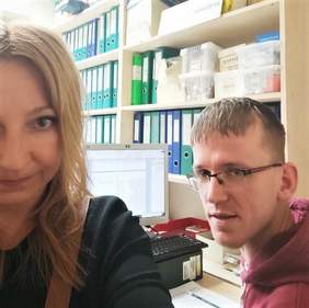 Pokaż zdjęcie: Na zdjęciu Pan Michał - uczestnik projektu oraz Pani Renata Czeronko - pośrednik pracy z ORK w Nałęczowie. Na pierwszym planie uśmiechnięte twarze dwóch osób. W tle komputer oraz regały z segregatorami
