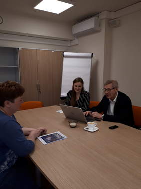 Pokaż zdjęcie: Trzy osoby siedzą przy stole konferencyjnym, na nim laptop i książka