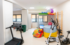 Pokaż zdjęcie: Sala ćwiczeń w której stoi bieżnia, rower stacjonarny, orbitrek. W sali są kolorowe pufy do ćwiczeń oraz drabinki na ścianie.