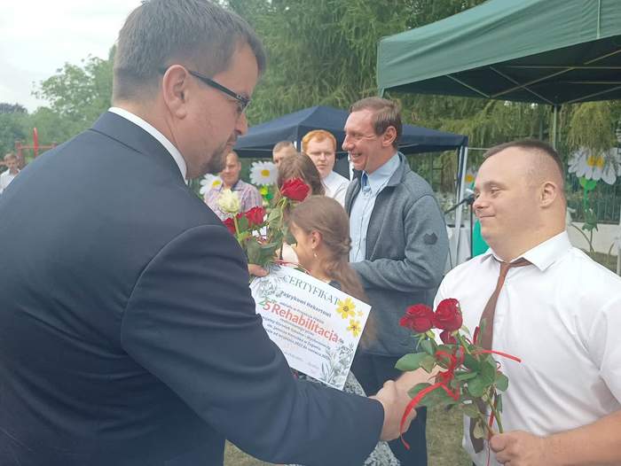 Pokaż zdjęcie: Dyrektor Oddziału Lubuskiego PFRON wręcza dyplom niepełnosprawnemu uczniowi i ściska mu rękę, oboje są zadowoleni i uśmiechnięci