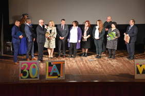 Kilkanaście osób na scenie, stoją w szeregu, jedna przemawia