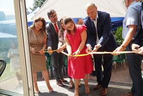 Pokaż zdjęcie: 6 osób, mężczyźni i kobiety przecinają wstęgę, słoneczny dzień