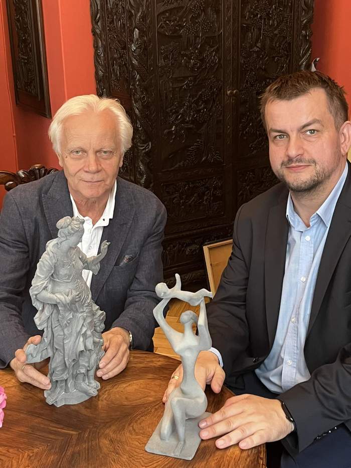 Pokaż zdjęcie: Dyrektor Oddziału Lubuskiego PFRON obok Dyrektora Muzeum Ziemi Lubuskiej w ZieloneJ Górze siedzą i trzymają w ręku eksponaty muzealne, są uśmiechnięci